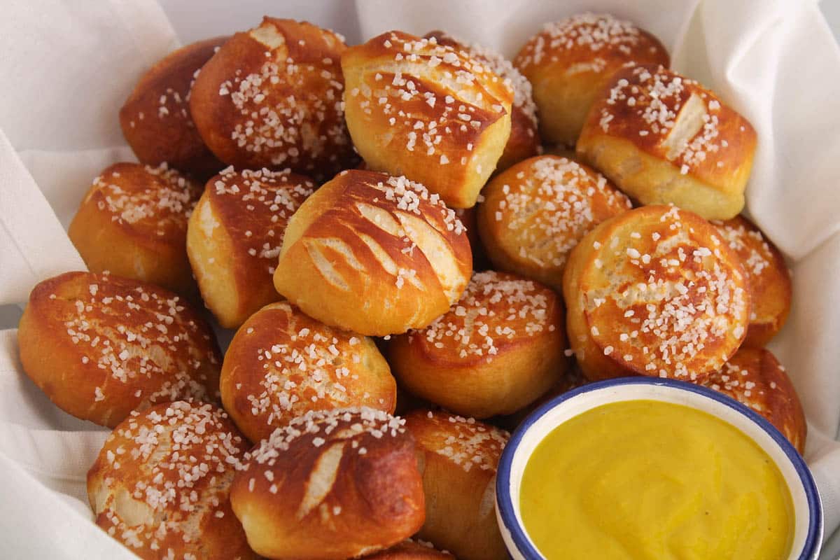 A pile of pretzel bites made with sourdough discard in a bowl with a white cloth and a side of mustard sauce.