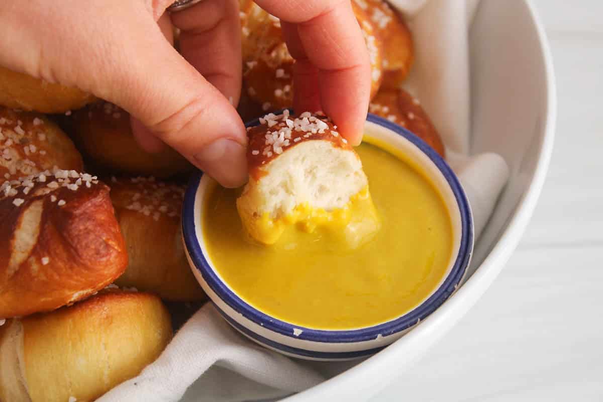 A halved pretzel bites dipping in a mustard sauce.