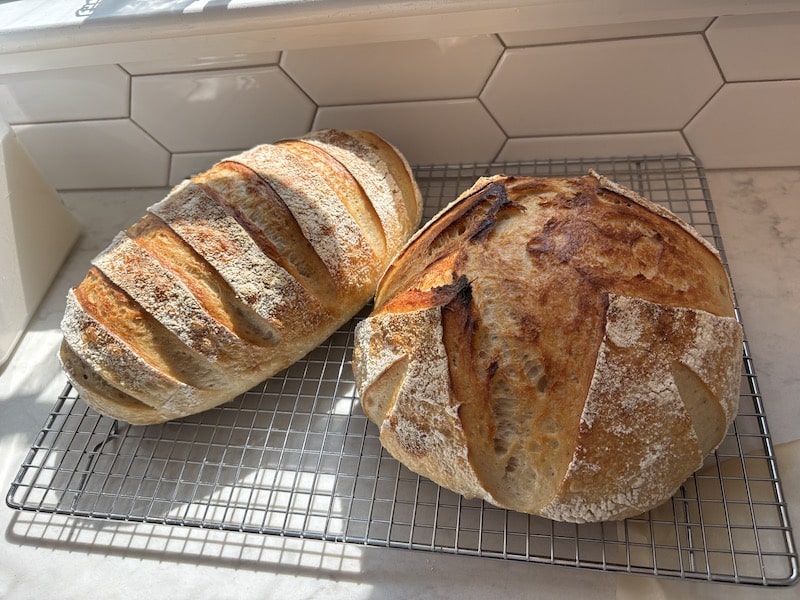 Two loaves of sourdough bread on a cooling rack on the counter.