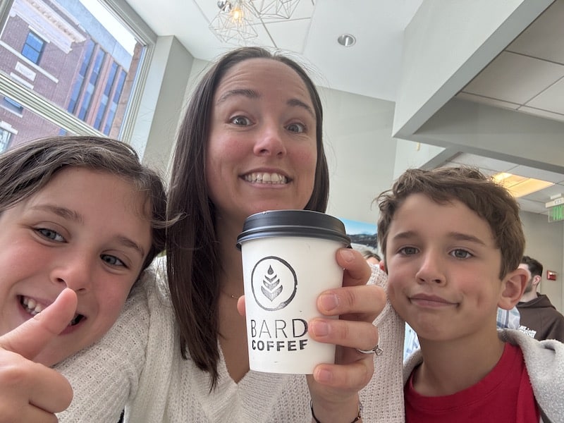 Jessica is holding a coffee with her children beside her.