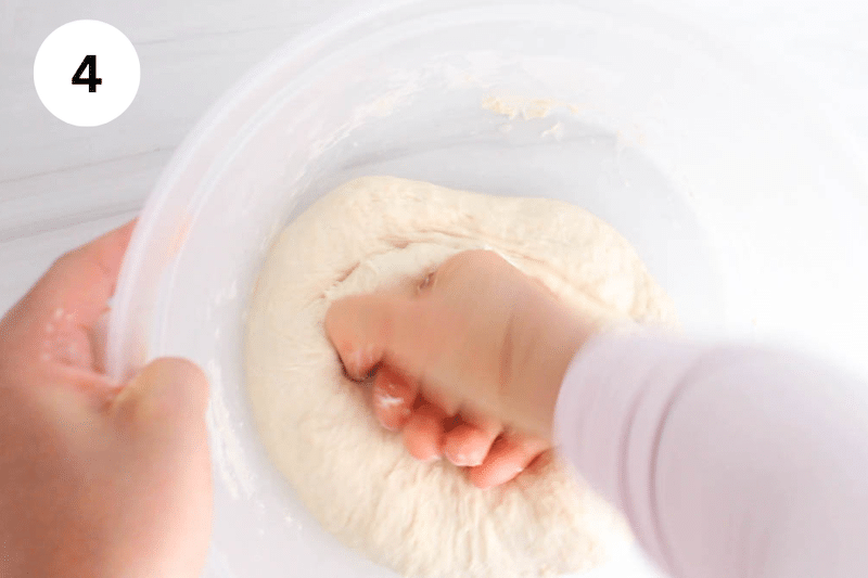 A hand kneading a dough in a large container.