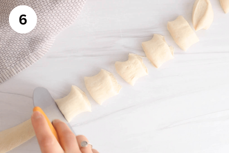 A dough cutter cutting a log of dough into bites.