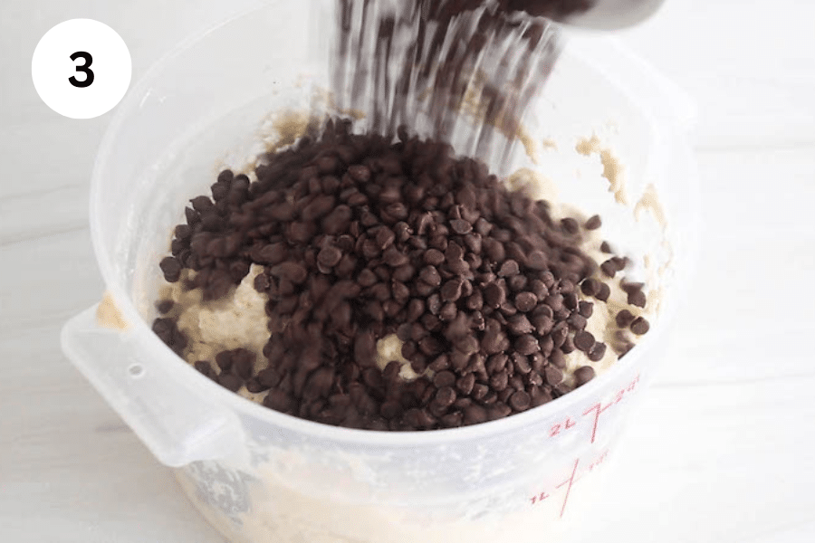 Chocolate chips pouring over a container with a dough.
