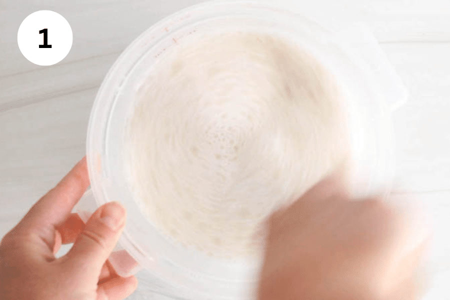 A container with hands mixing sourdough starter with water.