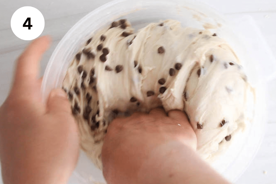 Hands kneading dough into a container.